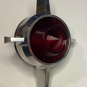 May include: A chrome and red tail light with four arms, resembling a star shape.