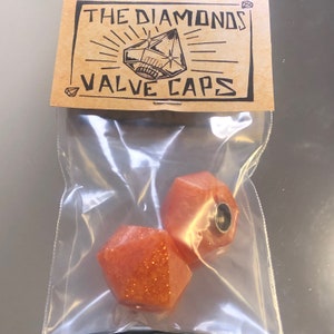 May include: Two orange diamond-shaped valve caps with a glittery finish. The caps are packaged in a clear plastic bag with a brown paper label that reads "The Diamonds Valve Caps".
