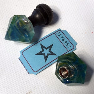 May include: Two blue and green resin gear shift knobs with a black knob on top of one. The knobs have a glittery finish. A blue ticket with the number 2176957 is in the background.