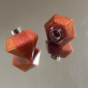 May include: Two brown, glittery, geometric resin bottle stoppers with a silver metal top. The stoppers are shaped like a diamond and a hexagon.
