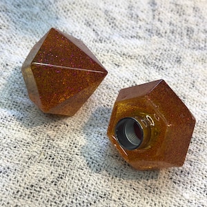 Può includere: Due tappi per bottiglie in glitter dorati con forma geometrica. Un tappo ha una forma di diamante e l'altro una forma esagonale. Entrambi i tappi hanno un'apertura filettata sul fondo.