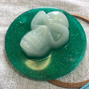 Peut inclure: Une décoration en résine en forme de crâne blanc sur un fond de paillettes vertes. Le crâne est translucide et a une finition brillante.