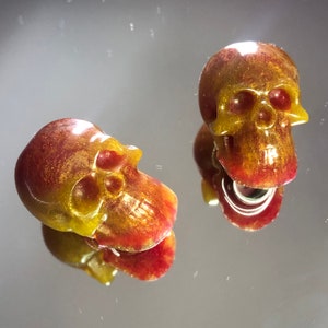 Peut inclure: Deux petits ornements en forme de crâne rouge et or pailleté.