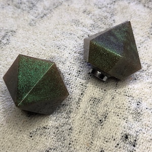 May include: Two dark green, geometrically shaped bottle stoppers with a glittery finish.