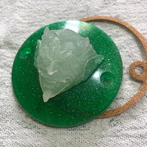 Peut inclure: Un disque rond en résine verte à paillettes avec une sculpture en résine transparente d'une tête de démon sur le dessus.