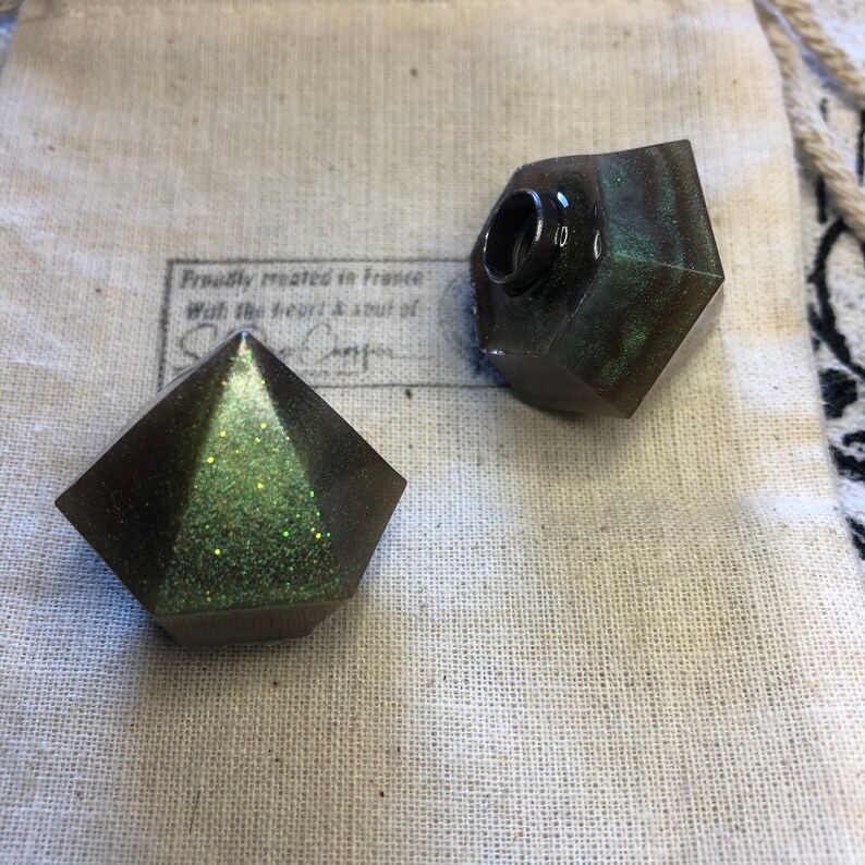 May include: Two green and black resin bottle stoppers with glitter. One stopper is a pyramid shape and the other is a rounded shape with a hole in the top.