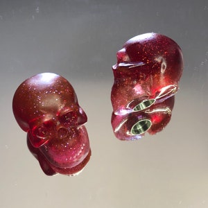 May include: Two red glitter skull bottle stoppers. The skulls are made of resin and have a sparkly finish.