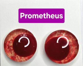 Puede incluir: Dos cabujones redondos de resina roja y dorada con un diseño blanco en forma de C. La palabra "Prometheus" se muestra en texto blanco sobre un rectángulo púrpura encima de los cabujones. Los cabujones tienen un acabado brillante.