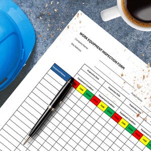 May include: A work equipment inspection form with a blue header and a grid for recording equipment condition. A black pen rests on the form, and a blue hard hat is visible. A cup of coffee sits in the upper right corner.