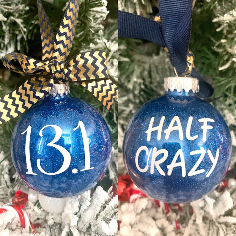 May include: Two blue glitter Christmas ornaments with white lettering. One ornament says "13.1" and the other says "HALF CRAZY".