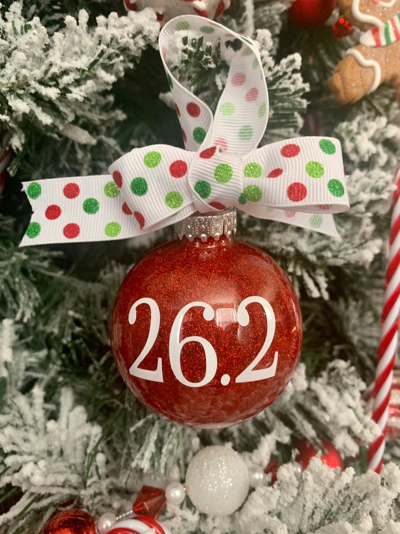 May include: Red glitter Christmas ornament with a white ribbon and white polka dots. The ornament has the number 26.2 written on it in white.
