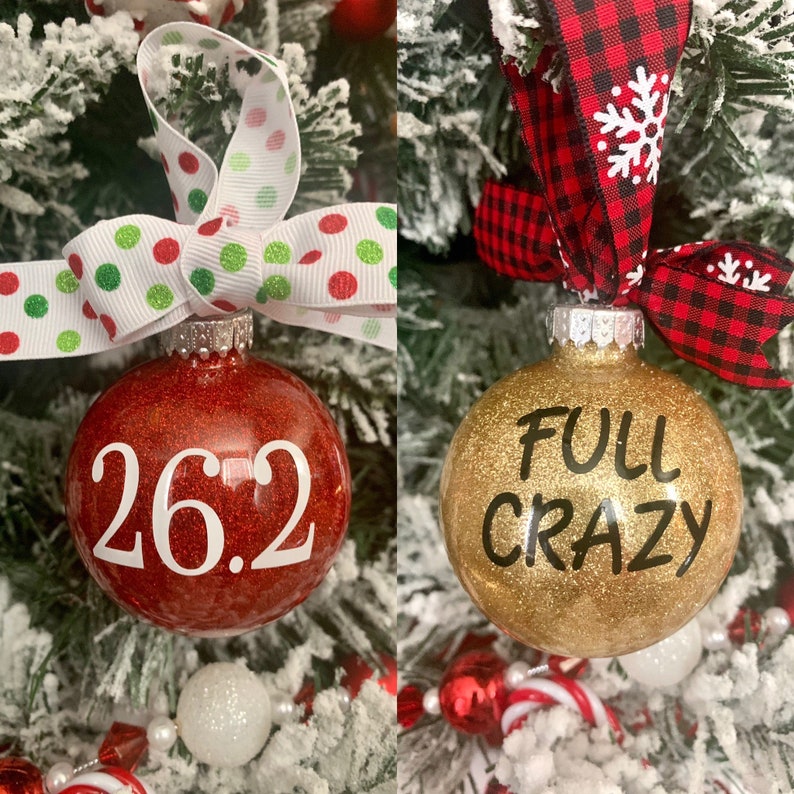 May include: Two Christmas ornaments, one red with white glitter and the text "26.2" and the other gold with black glitter and the text "FULL CRAZY".