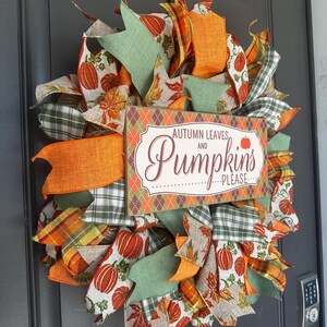 May include: A decorative wreath featuring orange, green, and white ribbons with pumpkin and leaf patterns. A rectangular wooden sign in the center displays the text Autumn Leaves and Pumpkins Please in brown and orange lettering on a cream background.