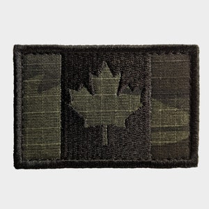 May include: A rectangular patch depicting the Canadian flag in a camouflage pattern. The maple leaf and stripes are in green and black hues, with a black border. This patch is likely for military or outdoor clothing and accessories.