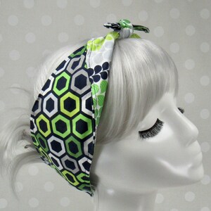 May include: A green, black, and white patterned headband with a geometric design. The headband is tied in a knot at the top of the head.