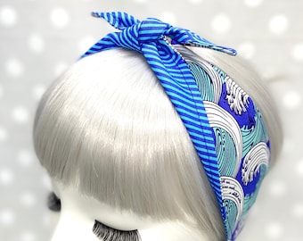 Puede incluir: Diadema azul y blanca con un patrón de olas. La diadema está anudada en la parte superior.