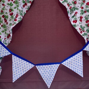 May include: A blue and white polka dot bunting with blue ribbon hanging in front of a window with red and white floral curtains.