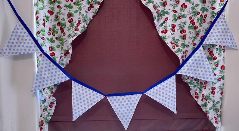 May include: A blue and white polka dot bunting with blue ribbon hanging in front of a window with red and white floral curtains.