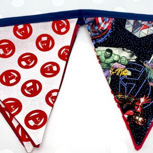 May include: A red and white fabric banner with a repeating pattern of the Avengers logo. The other side of the banner features a black background with images of the Avengers characters, including Hulk, Iron Man, and Captain America.