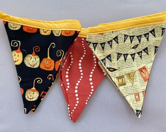 May include: Three fabric pennants with a yellow trim. The first pennant has a black background with orange and white jack-o-lantern faces. The second pennant has a red background with white polka dots. The third pennant has a cream background with black text that reads "Treat" and a black and white illustration of a bird.