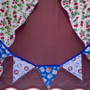May include: A blue and white fabric bunting with a blue trim. The bunting features a pattern of cartoon characters. The bunting is hanging from a white ceiling.