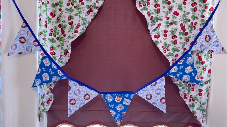 May include: A blue and white fabric bunting with a blue trim. The bunting features a pattern of cartoon characters. The bunting is hanging from a white ceiling.