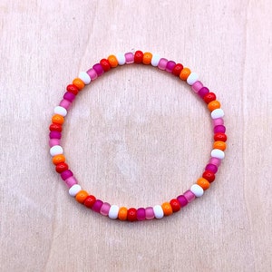 Puede incluir: Un brazalete de cuentas de colores con cuentas rosas, naranjas y blancas.
