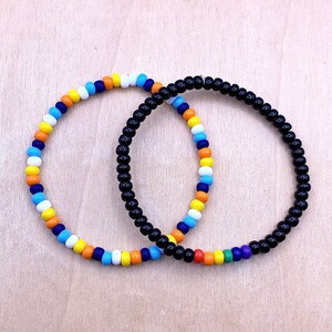 May include: Two beaded bracelets, one with black beads and the other with alternating blue, white, orange, and yellow beads.