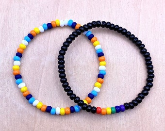 May include: Two beaded bracelets, one with black beads and the other with alternating blue, white, orange, and yellow beads.