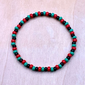 May include: A black, red, and green beaded bracelet. The beads are arranged in a repeating pattern.
