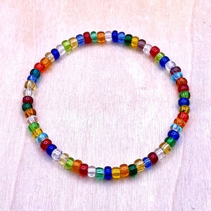 May include: A colorful beaded bracelet with alternating beads of red, orange, yellow, green, blue, and clear glass. The bracelet is made with small, round beads.