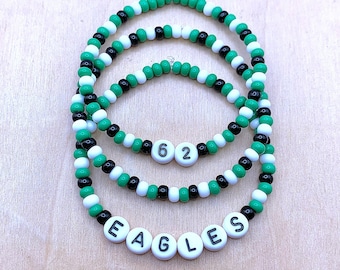 May include: Three green, white, and black beaded bracelets with the word "EAGLES" spelled out in white beads and the number "62" in white beads.