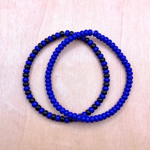 May include: Two beaded bracelets, one blue and black, the other solid blue.