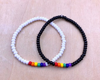 May include: Two beaded bracelets, one white and one black, with a rainbow of beads in the center.