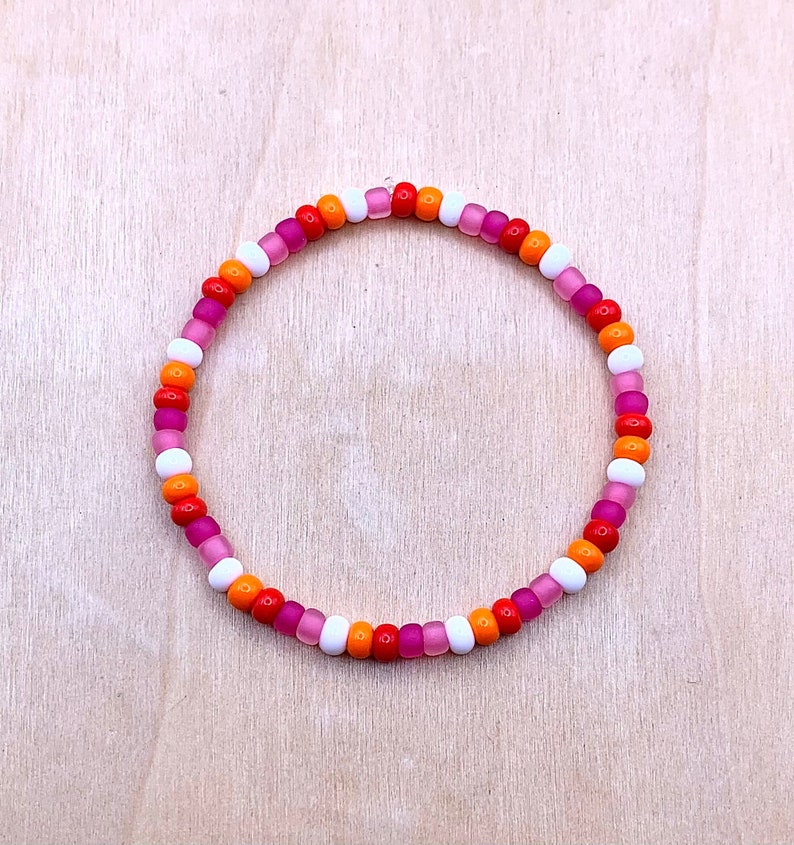 Puede incluir: Un brazalete de cuentas de colores con cuentas rosas, naranjas y blancas.