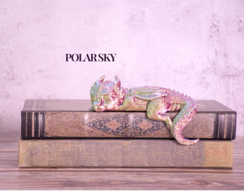 May include: A multi-colored dragon figurine rests on two antique books. The dragon has a pink, green, and blue color scheme. The books are brown with gold accents. The text "POLAR SKY" is above the books.