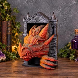 May include: A three-dimensional dragon sculpture emerging from a dark gray stone-textured archway. The dragon features vibrant orange and red scales, sharp horns, and a clawed hand extending from the base of the structure.