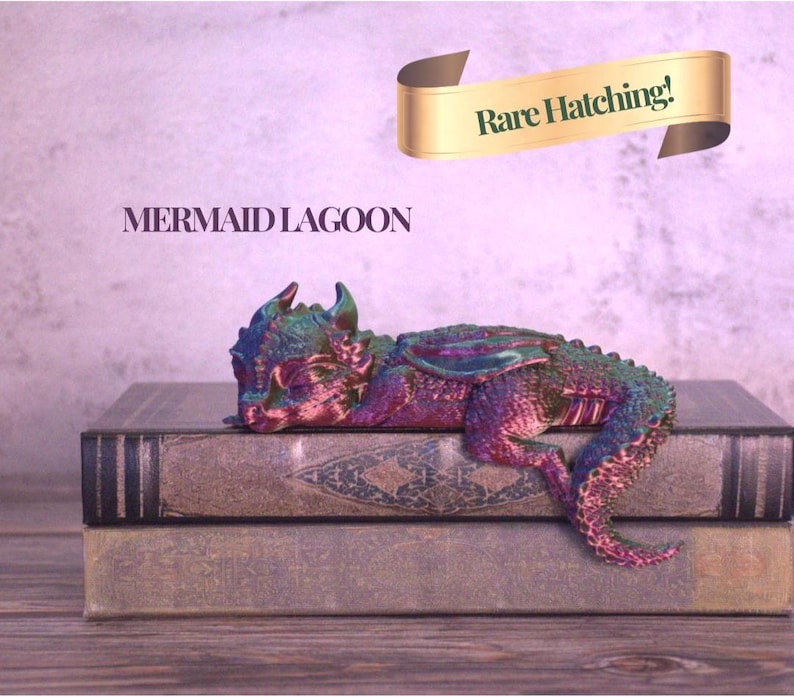 May include: A colorful, iridescent dragon figurine resting on two antique books. The dragon is primarily purple, green, and blue. The text "MERMAID LAGOON" is below the dragon, and a banner above reads "Rare Hatching!"