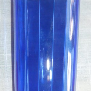 May include: A cobalt blue glass drinking glass with vertical ridges. The glass is empty and has a rounded bottom.