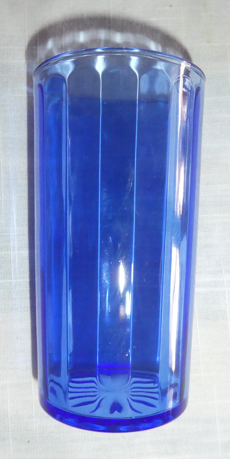 May include: A cobalt blue glass drinking glass with vertical ridges. The glass is empty and has a rounded bottom.
