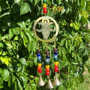 May include: A brass wind chime with a cutout of a human figure and three strands of colorful glass beads. Each strand has a bell at the bottom.