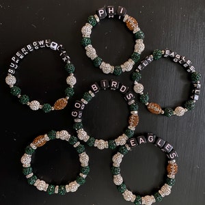 Könnte beinhalten: Sechs grüne und silberne Perlenarmbänder mit schwarzen Buchstabenperlen, die "SUPER BOWL", "GO BIRDS", "PHI", "FLY EAGLES", "EAGLES" und "FLY EAGLES" buchstabieren.