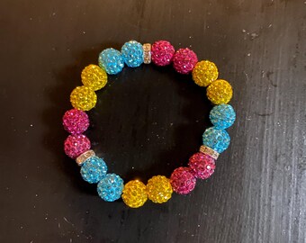 Può includere: Un braccialetto colorato con perline nei colori dell'arcobaleno: blu, giallo e rosa. Il braccialetto ha un design elastico ed è impreziosito da distanziatori color argento. Le perline rotonde hanno una superficie strutturata e scintillante. Circonferenza del polso: circa 17 cm.