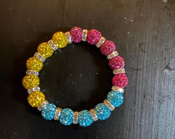 Può includere: Un braccialetto colorato con perline sferiche gialle, rosa e blu. Distanziatori color argento sono inseriti tra le perline. Un accessorio vivace.