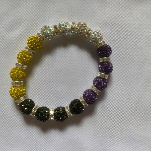 May include: A beaded bracelet with yellow, black, and purple beads. The beads are all round and have a sparkly finish.