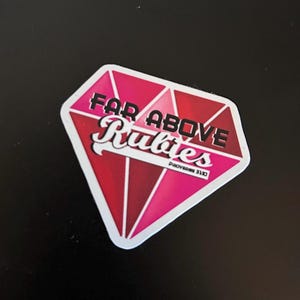 May include: A pink and red diamond-shaped sticker with the text "Far Above Rubies" and the scripture reference "Proverbs 31:10".