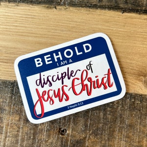 May include: A rectangular sticker with a blue border and the words "BEHOLD I AM A disciple of Jesus Christ" in white and red script. The sticker also includes the text "3 Nephi 5:13".