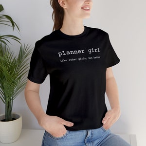 May include: Black t-shirt with white text that reads "planner girl like other girls, but better".