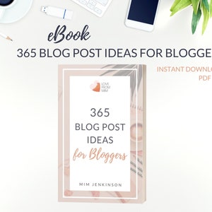 May include: A pink and white ebook cover with the title "365 Blog Post Ideas for Bloggers" and the subtitle "Instant Download PDF File". The cover features a pink heart with the text "Love From MM" and a floral design.