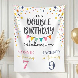 May include: A white fabric banner featuring colorful confetti and stars at the top, with the text IT'S A DOUBLE BIRTHDAY celebration. Below, it reads CONNIE is turning 7 and JACKSON is turning 9, accented by a small colorful bunting banner.